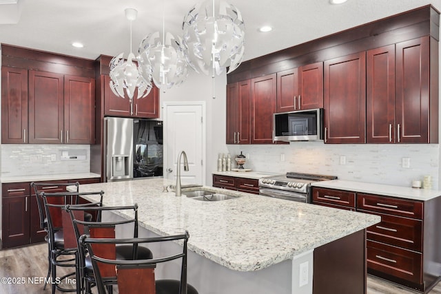 kitchen with reddish brown cabinets, appliances with stainless steel finishes, light stone counters, and a sink