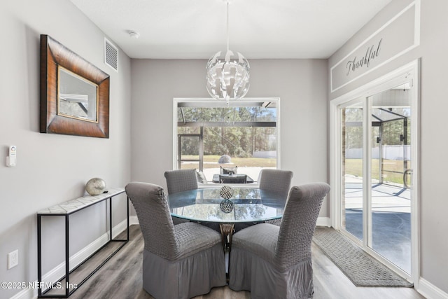 dining room with baseboards, wood finished floors, visible vents, and an inviting chandelier