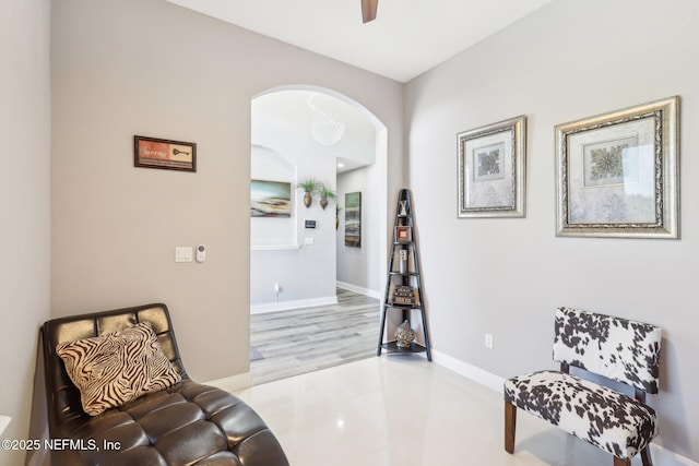 sitting room with arched walkways, tile patterned floors, a ceiling fan, and baseboards