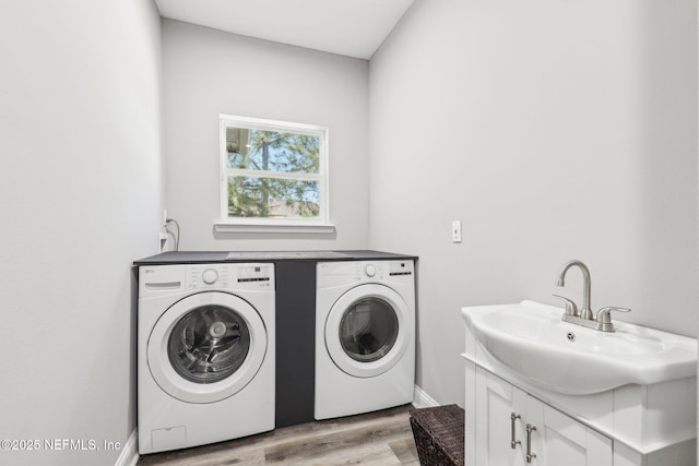 laundry room featuring washer and clothes dryer, cabinet space, light wood-style flooring, a sink, and baseboards