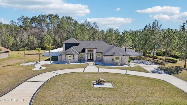 view of front of house featuring driveway, stone siding, a shingled roof, and a front lawn