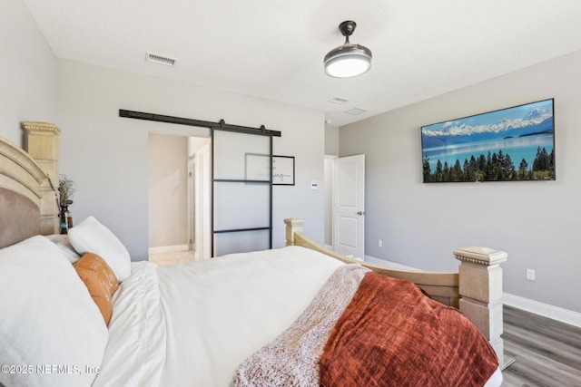 bedroom featuring a barn door, wood finished floors, visible vents, and baseboards