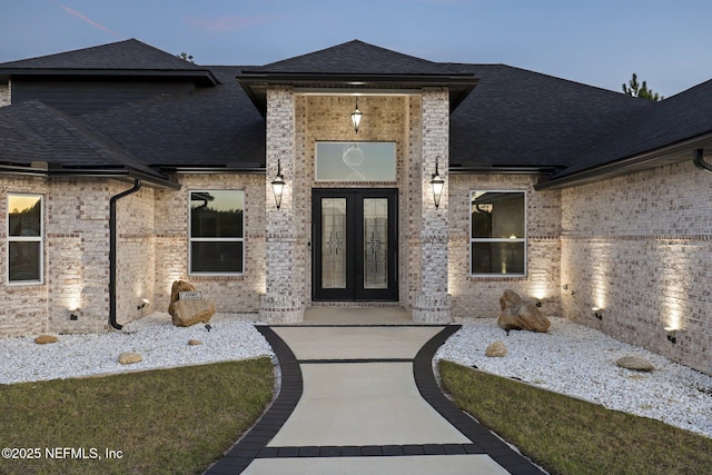 entrance to property featuring french doors, roof with shingles, and brick siding