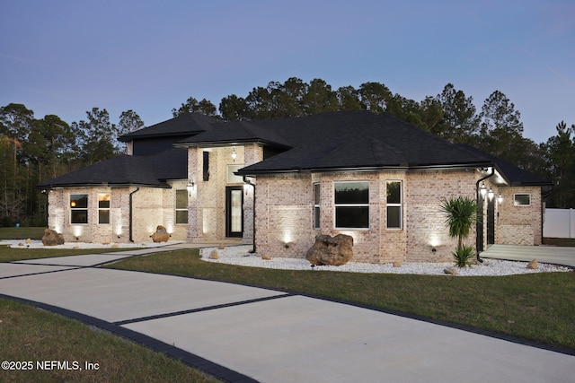 view of front facade featuring a shingled roof, a front lawn, concrete driveway, and brick siding