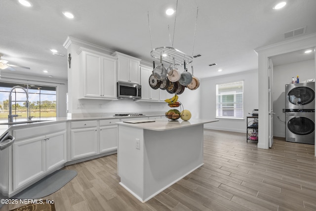 kitchen featuring stacked washing maching and dryer, a kitchen island, white cabinetry, sink, and stainless steel appliances