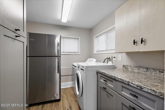 clothes washing area with washer and clothes dryer, cabinets, and light wood-type flooring