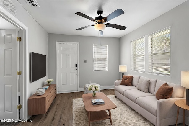 living room featuring visible vents, a ceiling fan, baseboards, and wood finished floors