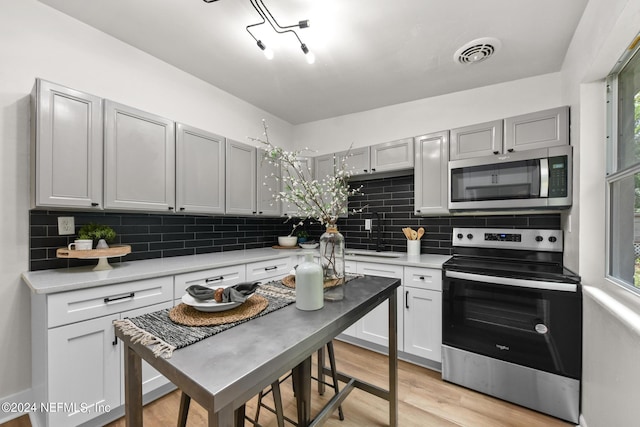 kitchen featuring sink, gray cabinets, stainless steel appliances, decorative backsplash, and light wood-type flooring