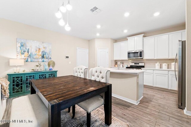 kitchen featuring light wood-type flooring, pendant lighting, stainless steel appliances, a kitchen island with sink, and white cabinets