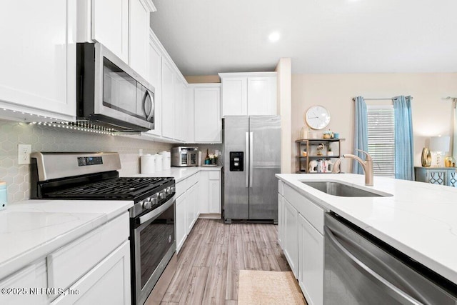 kitchen with sink, appliances with stainless steel finishes, white cabinets, light stone countertops, and backsplash