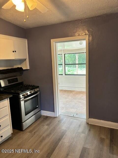 kitchen featuring stainless steel gas range, light wood-style flooring, white cabinetry, and a textured ceiling