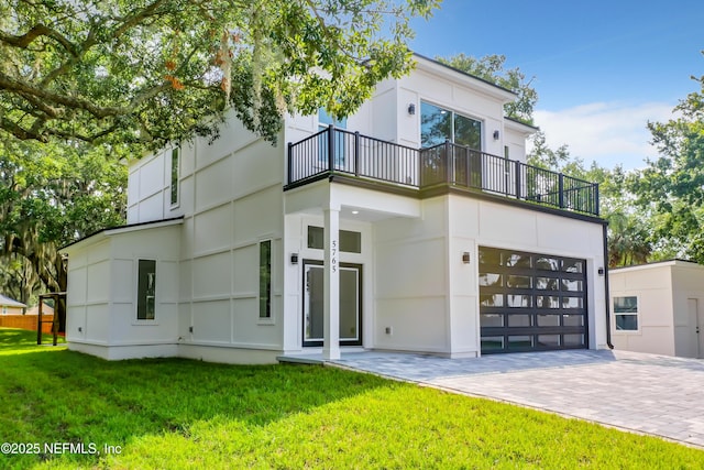 rear view of property featuring a garage, a balcony, and a yard