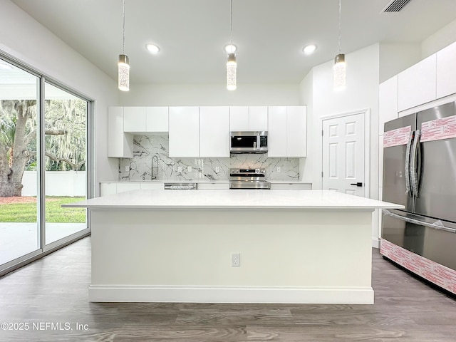 kitchen with white cabinetry, hanging light fixtures, stainless steel appliances, and a center island