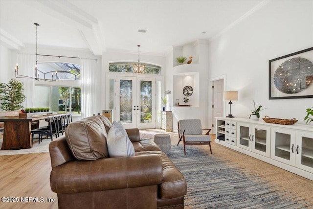 living room featuring an inviting chandelier, hardwood / wood-style floors, a towering ceiling, ornamental molding, and french doors