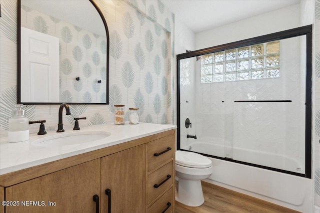 full bathroom featuring hardwood / wood-style flooring, vanity, combined bath / shower with glass door, and toilet