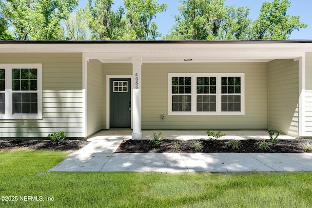 view of exterior entry featuring a yard and covered porch