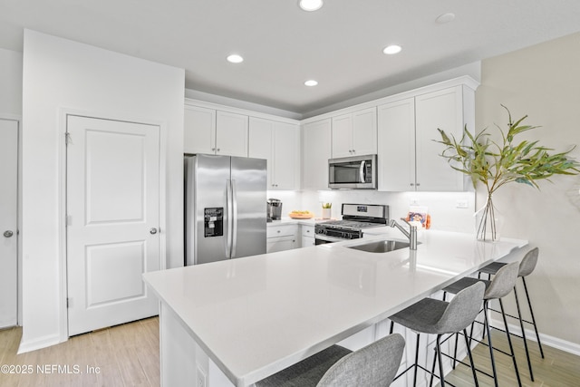 kitchen featuring stainless steel appliances, a sink, a peninsula, and light wood-style flooring