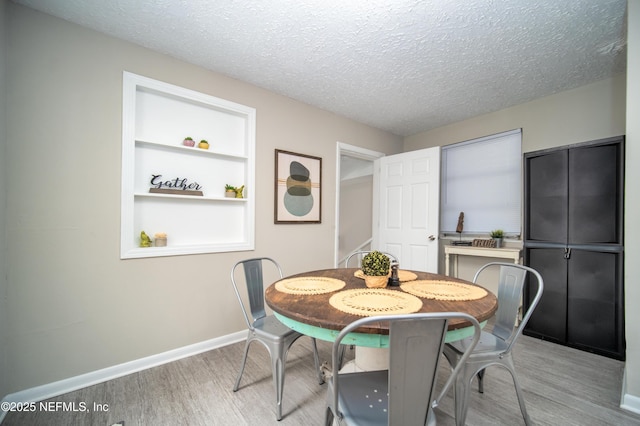 dining space featuring a textured ceiling, baseboards, built in features, and light wood-style floors