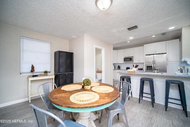 dining space featuring baseboards, visible vents, a textured ceiling, light wood-type flooring, and recessed lighting