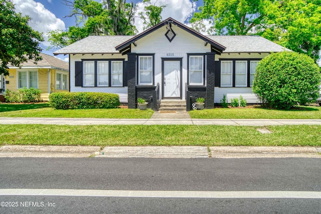 bungalow with entry steps, roof with shingles, and a front lawn