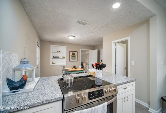 kitchen with a textured ceiling, stainless steel electric range, visible vents, and white cabinets