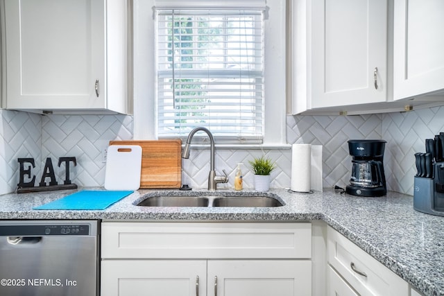 kitchen featuring tasteful backsplash, dishwasher, light stone countertops, white cabinetry, and a sink