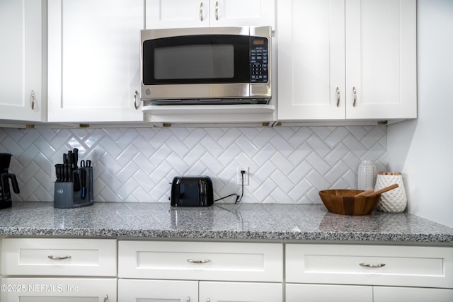 kitchen featuring stainless steel microwave, backsplash, light stone countertops, and white cabinets