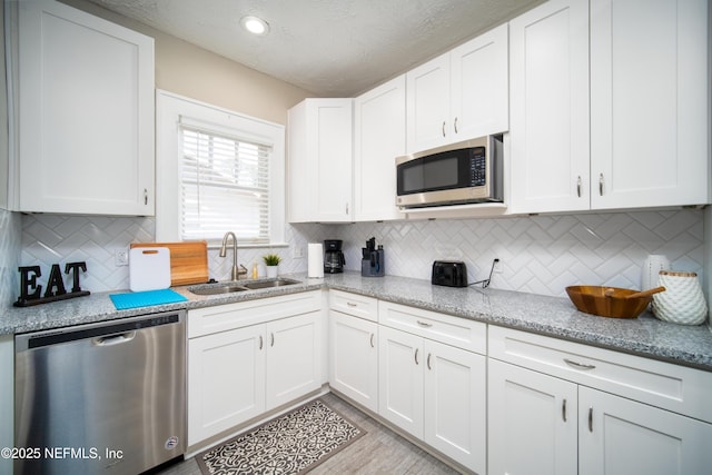 kitchen with appliances with stainless steel finishes, decorative backsplash, a sink, and white cabinets