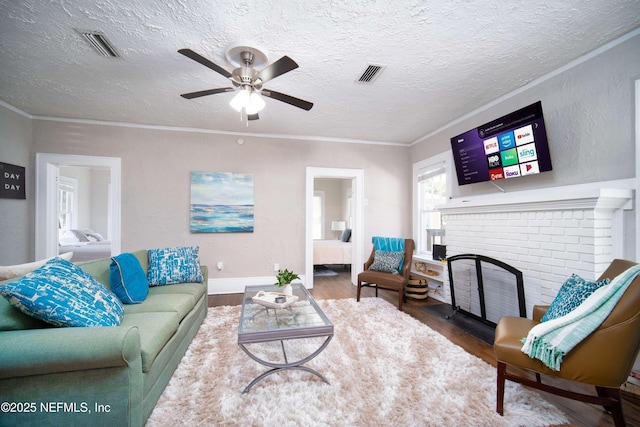 living area with visible vents, ornamental molding, a brick fireplace, a textured ceiling, and wood finished floors