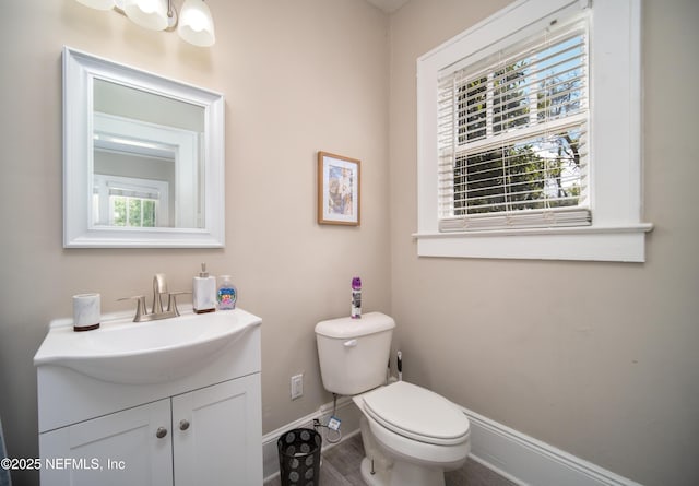 half bath with baseboards, vanity, and toilet