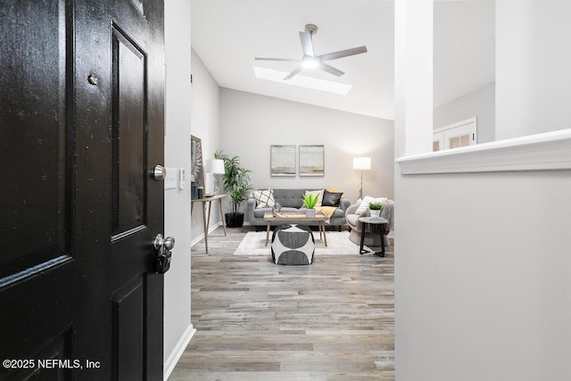 entrance foyer featuring vaulted ceiling with skylight, wood finished floors, a ceiling fan, and baseboards