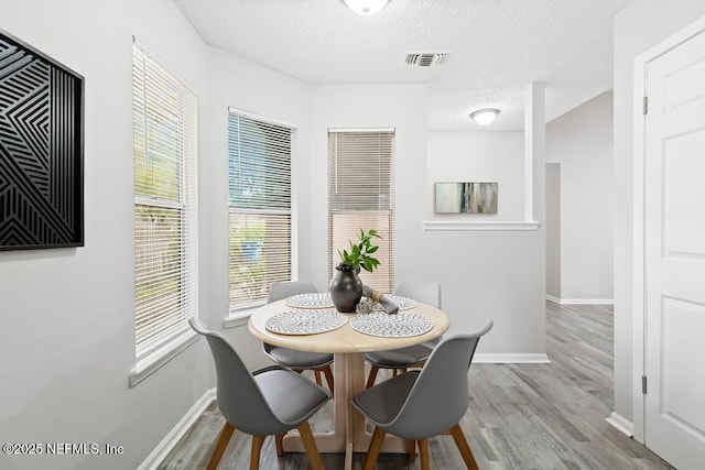 dining space with visible vents, a textured ceiling, baseboards, and wood finished floors