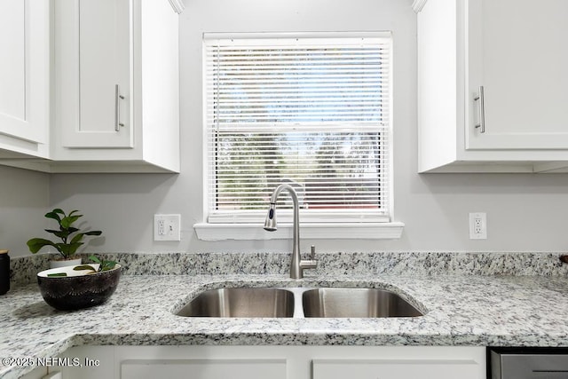 kitchen featuring light stone countertops, white cabinets, and a sink