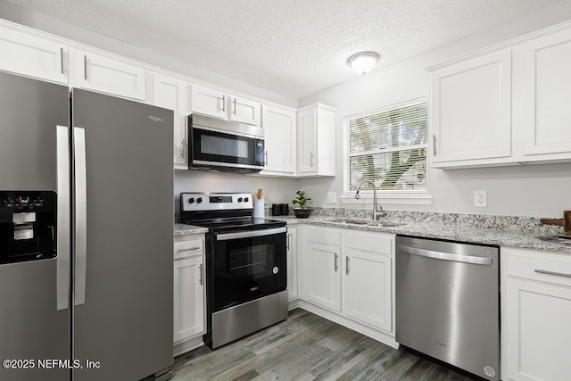 kitchen with appliances with stainless steel finishes, white cabinetry, a sink, a textured ceiling, and light wood-type flooring