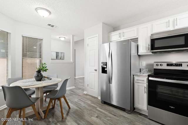 kitchen featuring a textured ceiling, white cabinetry, visible vents, light wood-style floors, and appliances with stainless steel finishes