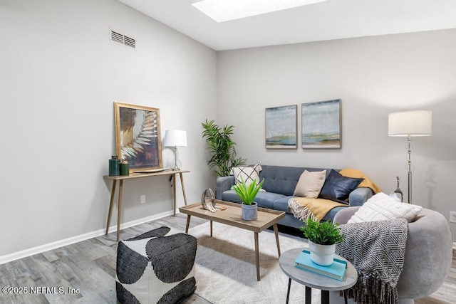 living area featuring a skylight, baseboards, visible vents, and wood finished floors