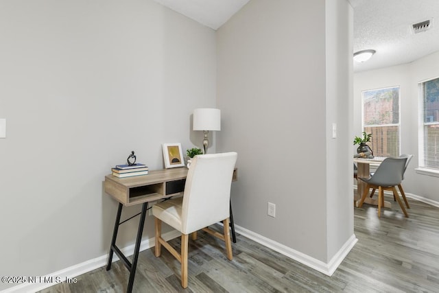 office with a textured ceiling, wood finished floors, visible vents, and baseboards