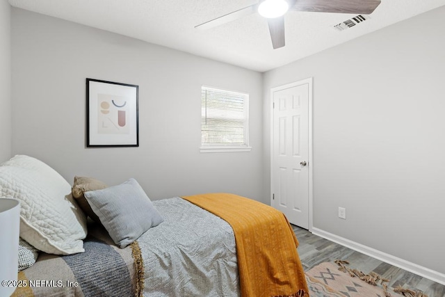 bedroom featuring a ceiling fan, visible vents, baseboards, and wood finished floors