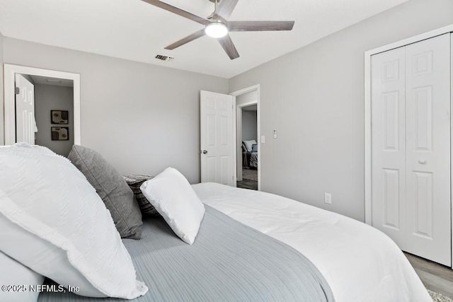 bedroom with ceiling fan, visible vents, a closet, and wood finished floors