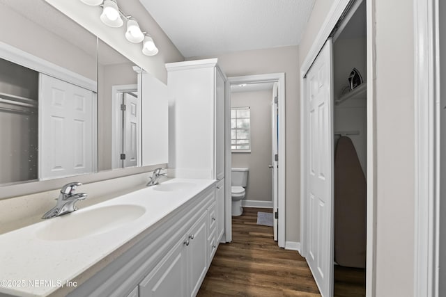 full bath featuring double vanity, wood finished floors, toilet, and a sink