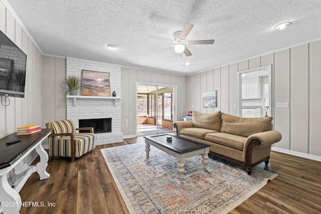 living area featuring crown molding, ceiling fan, a fireplace, dark wood-style floors, and a textured ceiling