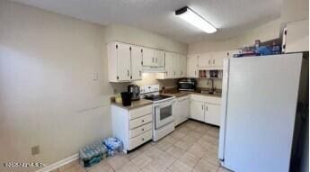 kitchen with white appliances, under cabinet range hood, white cabinets, and a sink