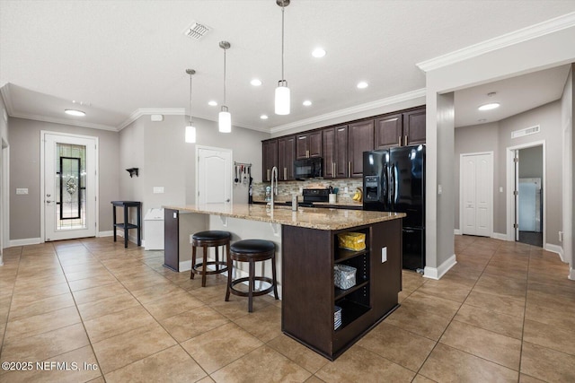 kitchen with light stone counters, dark brown cabinets, an island with sink, pendant lighting, and black appliances