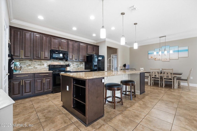 kitchen with decorative light fixtures, dark brown cabinets, black appliances, and an island with sink