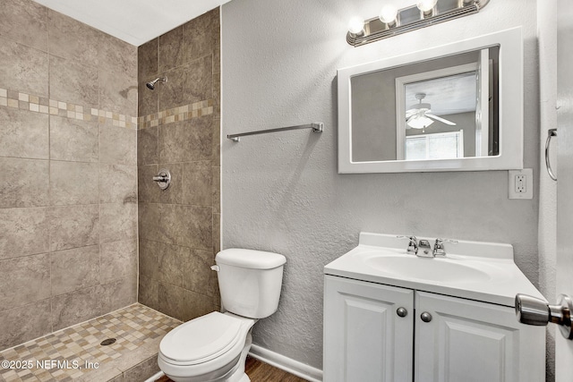 bathroom featuring ceiling fan, tiled shower, vanity, wood-type flooring, and toilet