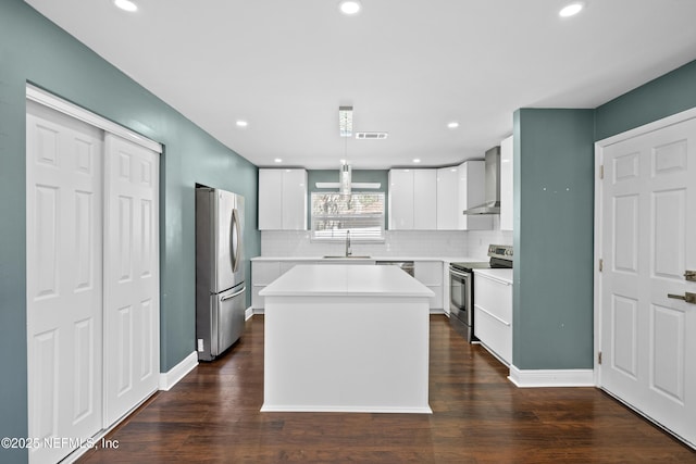 kitchen featuring wall chimney exhaust hood, white cabinetry, a center island, hanging light fixtures, and stainless steel appliances