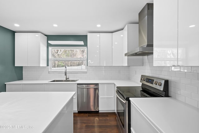 kitchen with wall chimney range hood, sink, appliances with stainless steel finishes, white cabinetry, and dark hardwood / wood-style floors