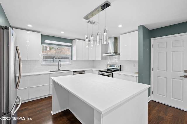 kitchen featuring stainless steel appliances, a kitchen island, wall chimney range hood, and white cabinets