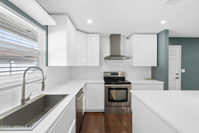 kitchen featuring wall chimney range hood, sink, white cabinets, and appliances with stainless steel finishes