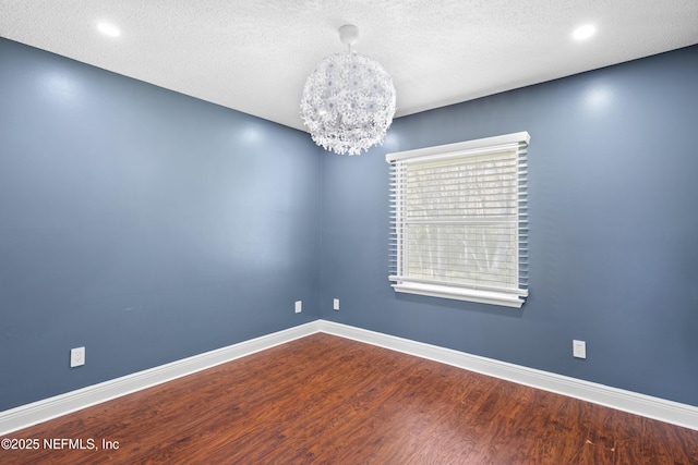 unfurnished room featuring a notable chandelier, hardwood / wood-style flooring, and a textured ceiling